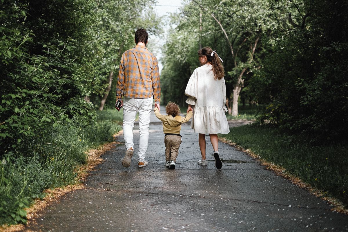 Un couple et un jeune enfant se promènent sur une allée arborée, vus de dos