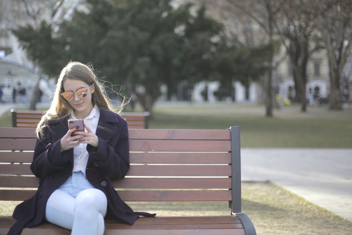 Une femme regarde son téléphone, assise sur un banc dans un parc