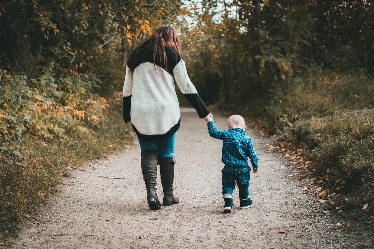 Mama i jej syn idą za rękę leśną ścieżką, widziani od tyłu