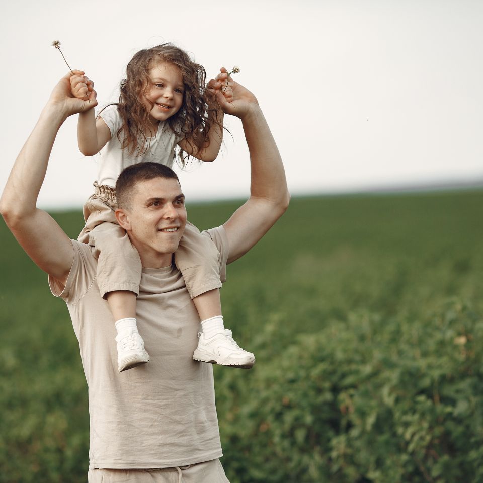 Un papa porte sa fille sur ses épaules dans un champ